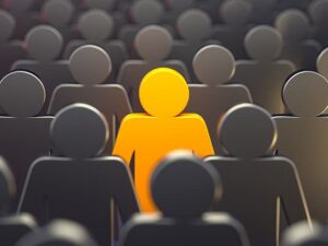 A group of grey humanoid figures with one standing out in bright orange in the center. The image symbolizes individuality and uniqueness.